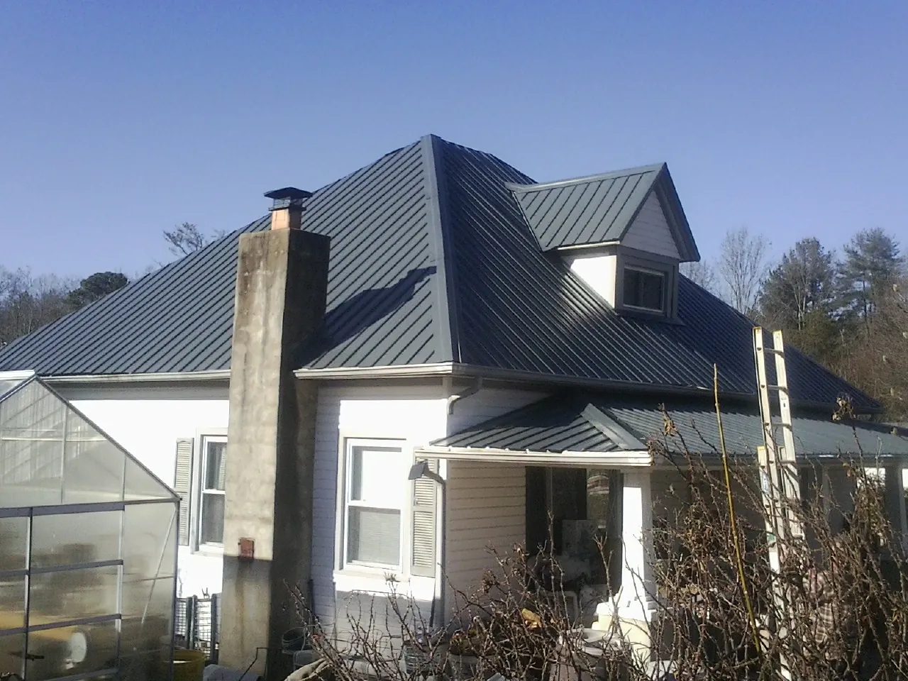 Dark blue standing seam metal roof on a white farmhouse with dormer — Slate & Tile Roof Repair by Roofing Brothers in Burkburnett