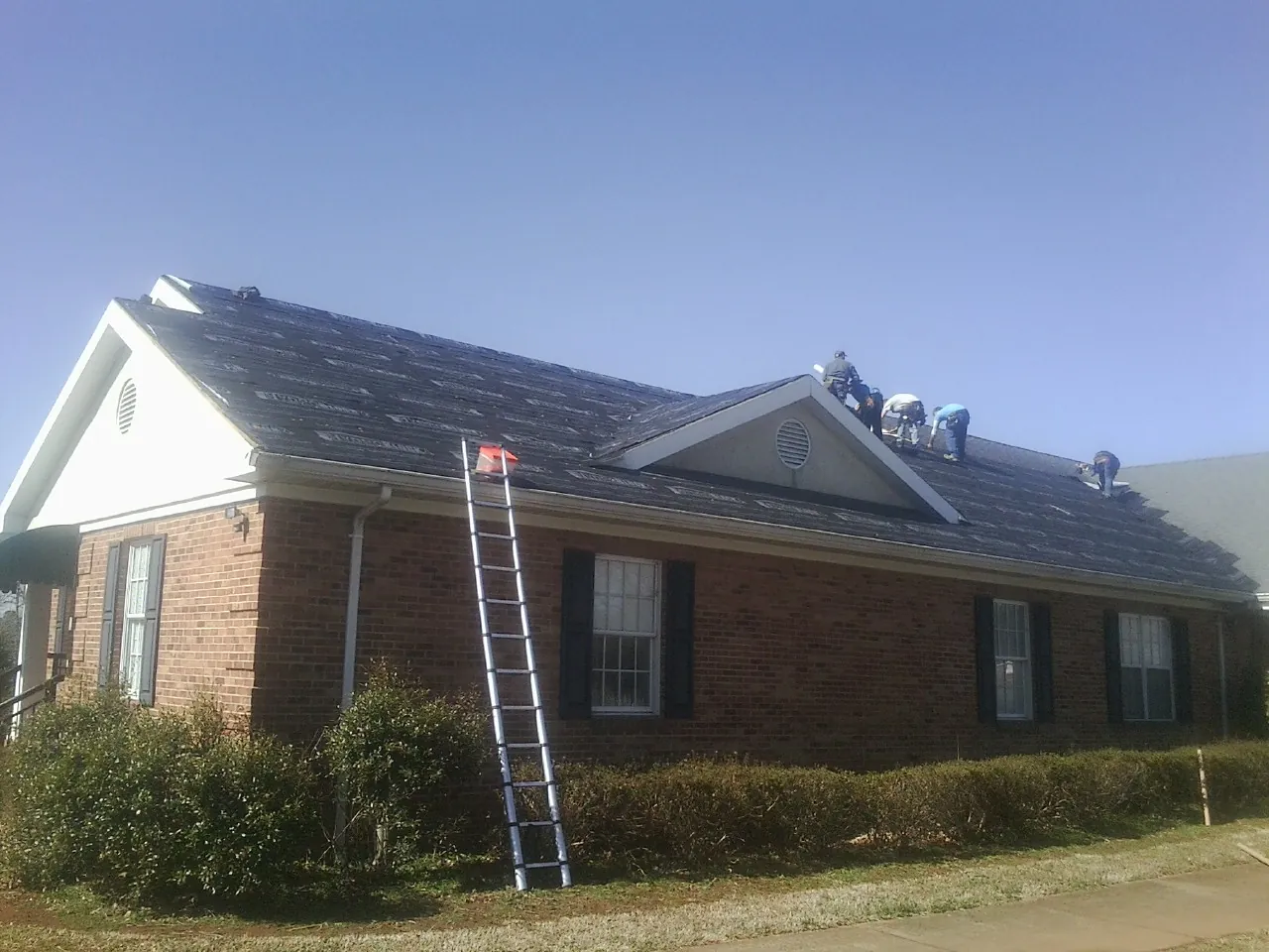 Crew tearing shingles off a brick ranch roof with a ladder set — Metal Roof Repair work by our crew in Burkburnett