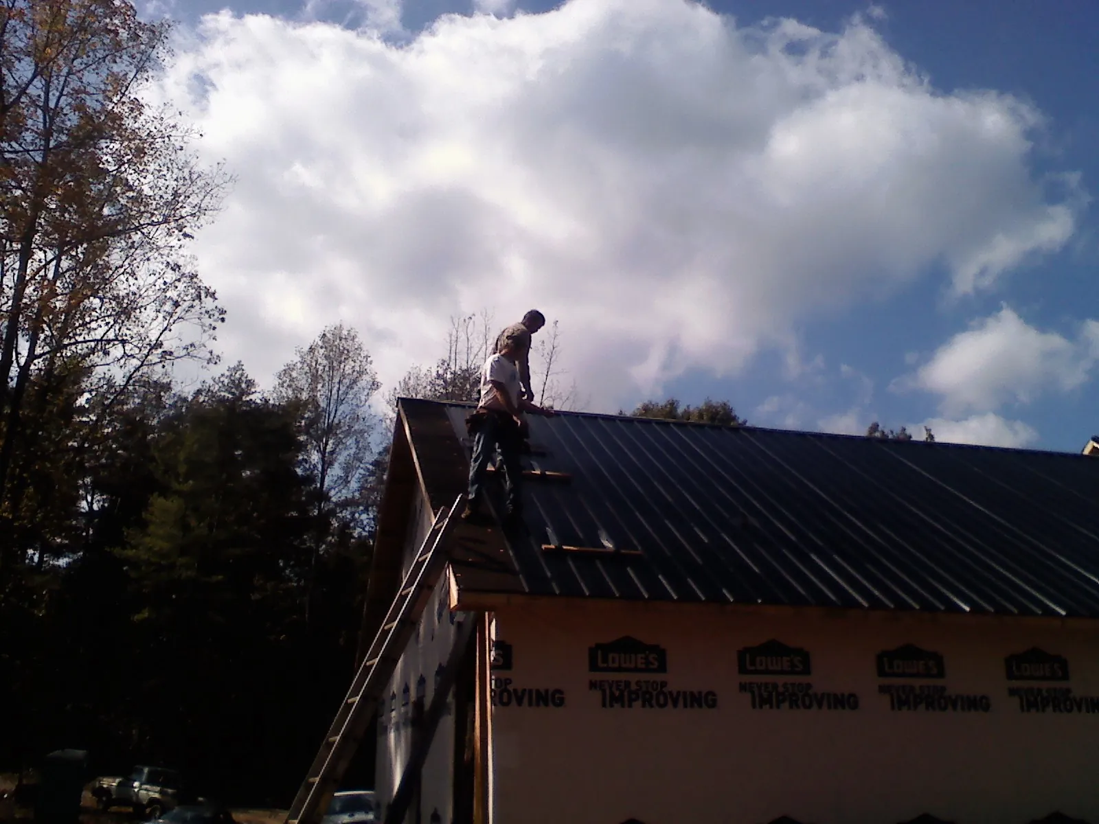 Roofer fastening dark metal panels high against a cloudy sky, from a Roof Inspection job in Burkburnett