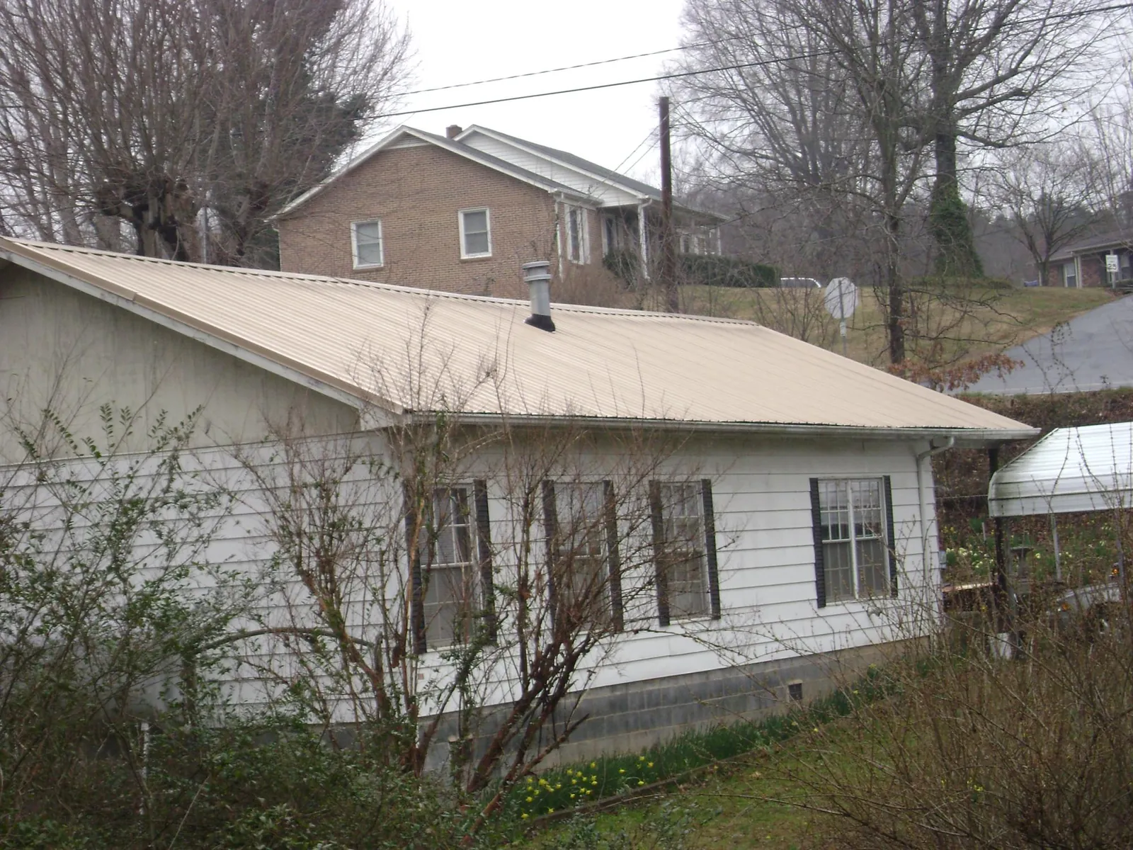 Tan metal roof on a white sided house set into a hillside — Commercial Roofing by Roofing Brothers in Burkburnett