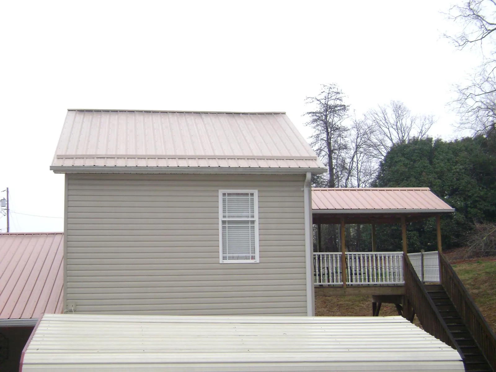 Tan metal roofs on a two story addition and attached porch, from a Roof Replacement job in Burkburnett
